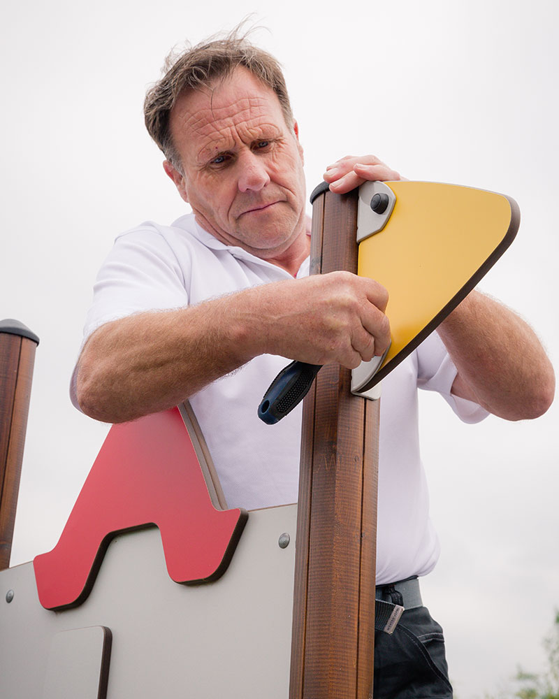 A HAGS Employee is fixing a playground unit at a park using a wrench to tighten bolts.